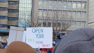 Protest sign saying "Open your eyes, mind, heart." 