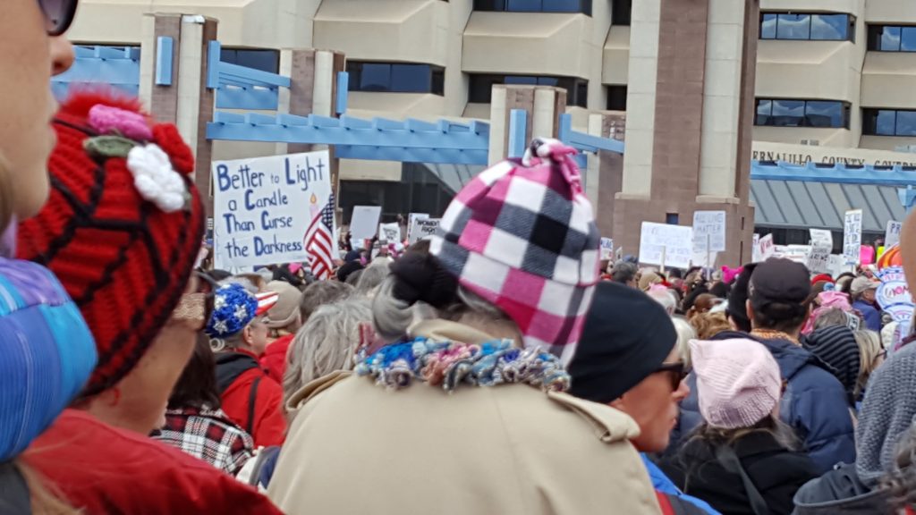 Protest march showing sign reading "Better to Light a Candle than Curse the Darkness"